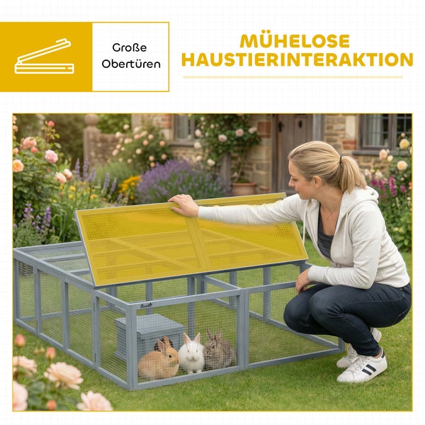 Eine Frau öffnet die große Obertür eines grauen Kleintiergeheges aus Holz und Draht auf einem Rasen mit drei Kaninchen für einfache Interaktion.