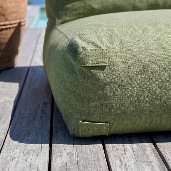 Nahaufnahme eines strukturierten grünen Bodenkissens auf einer hellen Holzterrasse neben einem Terrakottatopf.