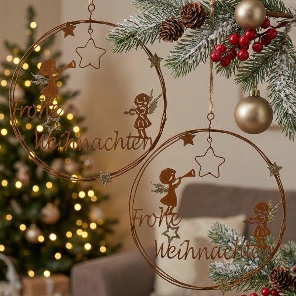 Zwei runde Metallhänger mit Engel-Motiven und dem Schriftzug Frohe Weihnachten als festliche Weihnachtsdekoration vor einem Weihnachtsbaum.