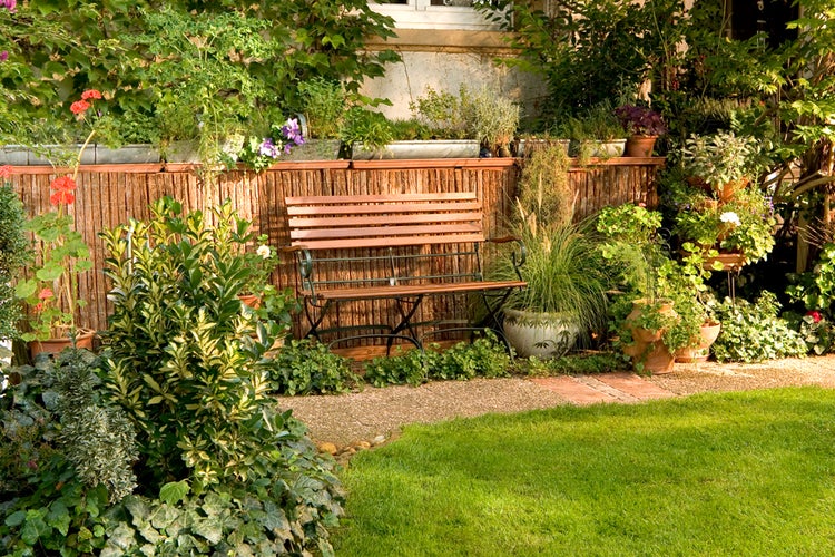 Gartenszene mit Holzzaun, Bank, Pflanzen und Rasenfläche