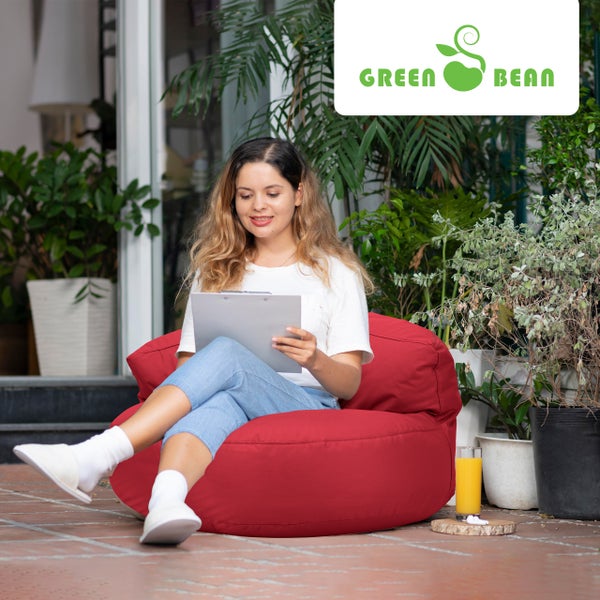 Eine Frau sitzt auf einem Sitzsack im Freien und liest ein Dokument. Im Hintergrund befinden sich Pflanzen und das Green Bean Logo.