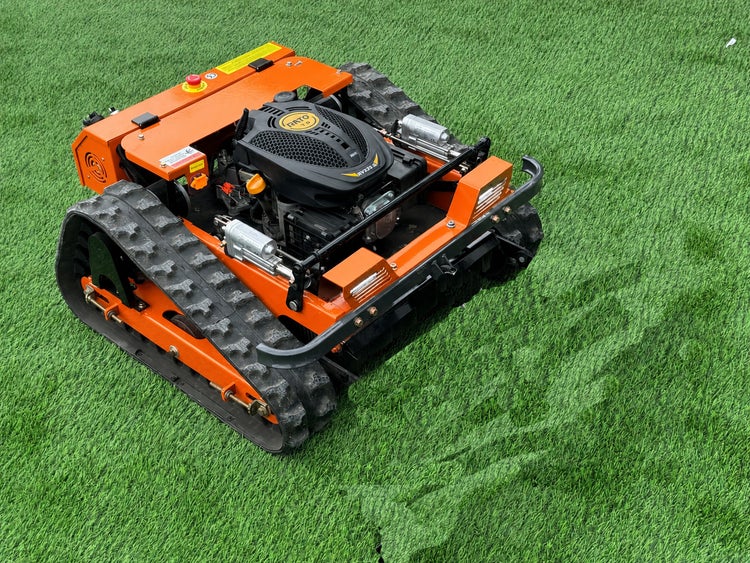 Oranger ferngesteuerter Böschungsmäher mit schwarzen Kettenantrieben und Benzinmotor auf einer Rasenfläche.