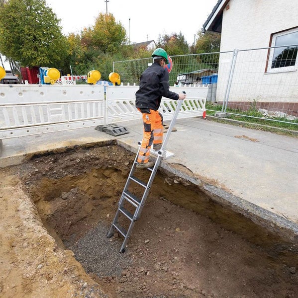 Aluminium-Grabenleiter mit Haltebügel im Einsatz an einer Baugrube mit einem Arbeiter.
