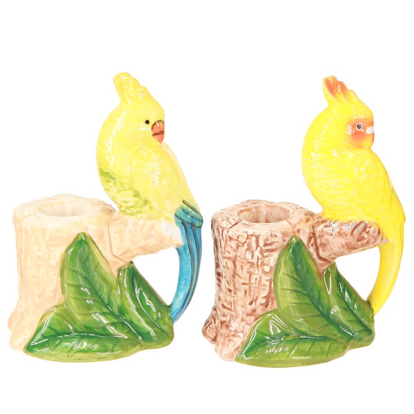 Zwei dekorative Kerzenhalter, jeweils mit einem gelben Kakadu auf einem Baumstumpf und grünen Blättern