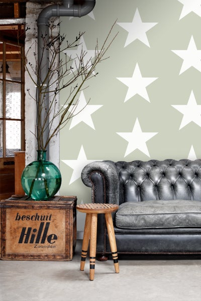 Interieuransicht mit einem Sofa, einem Hocker und einer Holzkiste vor einer Wand mit Sternenmuster