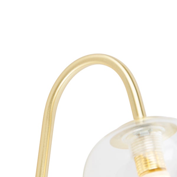 Detailaufnahme einer Lampe mit goldenem Gestell und transparentem Glasschirm
