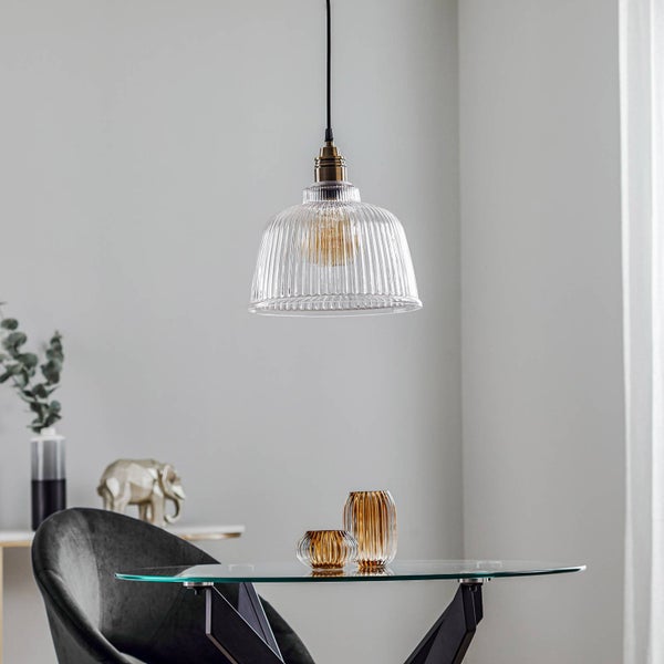 Pendelleuchte mit geriffeltem Glasschirm und Metallfassung über einem Glastisch in einem hellen, modern eingerichteten Raum.