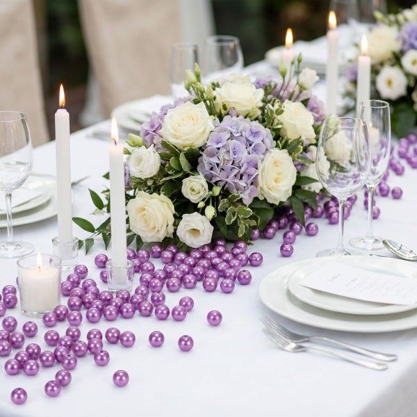 Festlich gedeckter Esstisch mit Blumenarrangement aus Rosen und Hortensien, Stumpenkerzen, Stielgläsern und dekorativen Perlen zur Tischdekoration.
