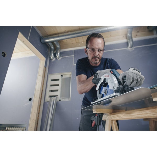 Handwerker bei der Arbeit mit einer Bosch Kreissäge zum Zuschneiden von Metall auf einer Holzunterlage in einem Raum.