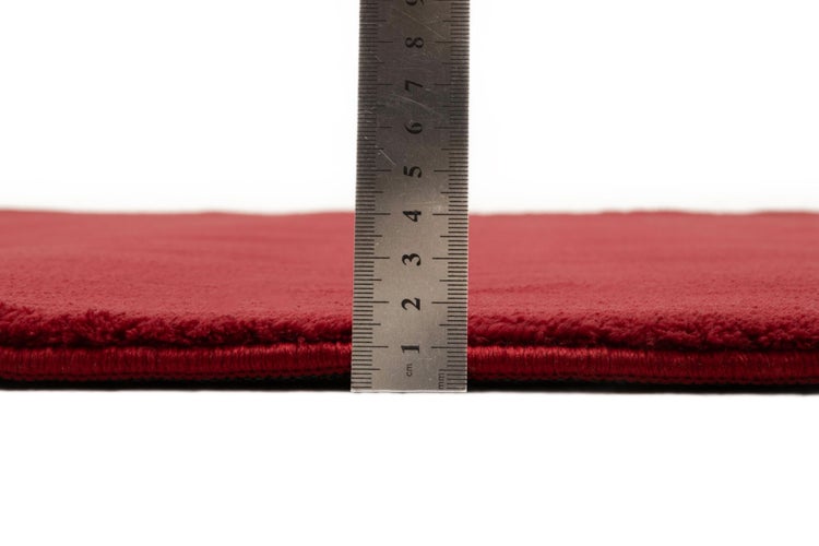 Roter Teppich mit einer Florhöhe von circa 1 Zentimeter, gemessen mit einem Metalllineal.