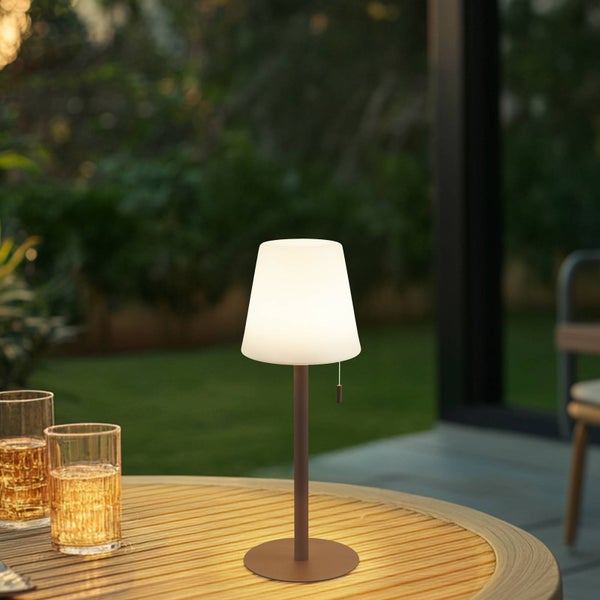 Moderne LED-Tischleuchte für außen mit weißem Schirm und braunem Gestell auf einem runden Holztisch im Garten bei Dämmerung.