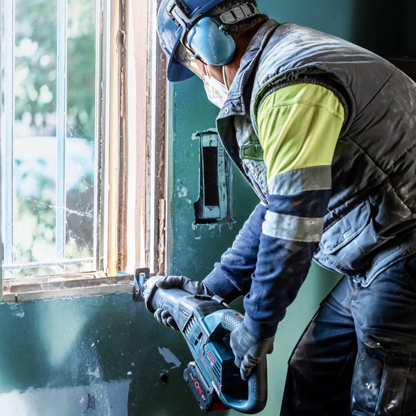 Ein Bauarbeiter demontiert mit einer Säbelsäge ein Fenster.
