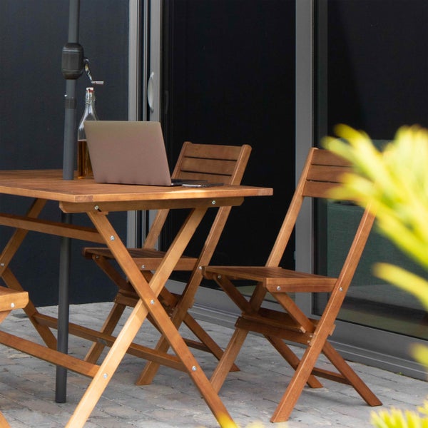 Klappbarer Gartentisch und Klappstühle aus Holz auf einer Terrasse mit Laptop.