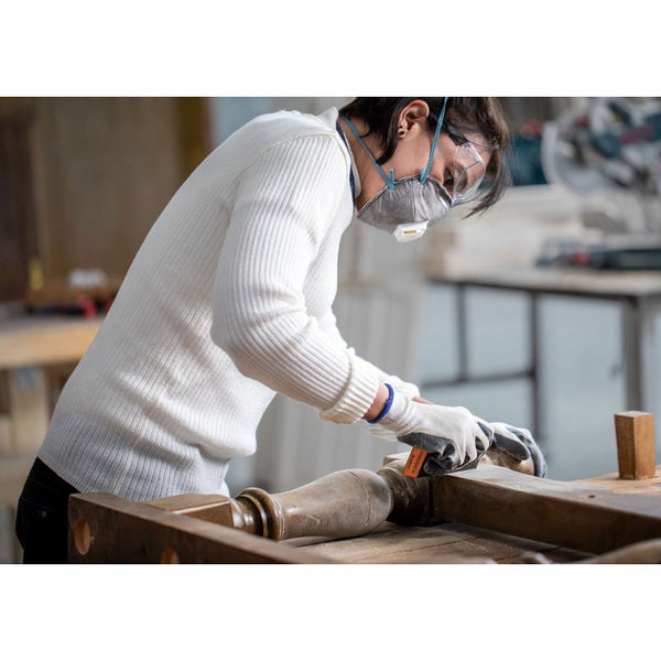 Frau schleift Holz mit Schleifpapier, ausgestattet mit Schutzbrille und Staubschutzmaske.