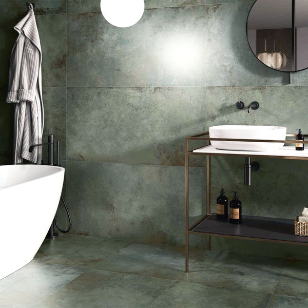 Modernes Badezimmer mit großformatigen Fliesen in grüner Metalloptik an Wand und Boden, freistehender Badewanne, Aufsatzwaschbecken und Rundspiegel.