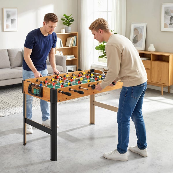 Zwei Männer spielen Tischkicker an einem stabilen Kickertisch aus Holz in einem hellen, modern eingerichteten Wohnzimmer.