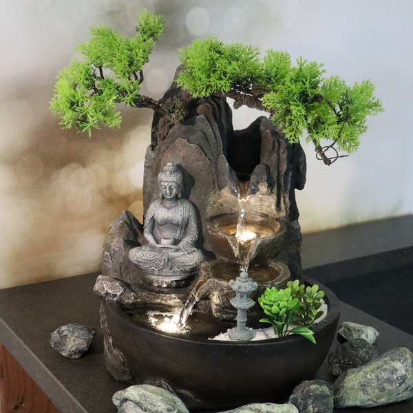 Zimmerbrunnen mit Buddha-Statue, künstlichem Bonsai-Baum, Felsen, Beleuchtung, Wasserfall und Laterne in runder, schwarzer Schale.