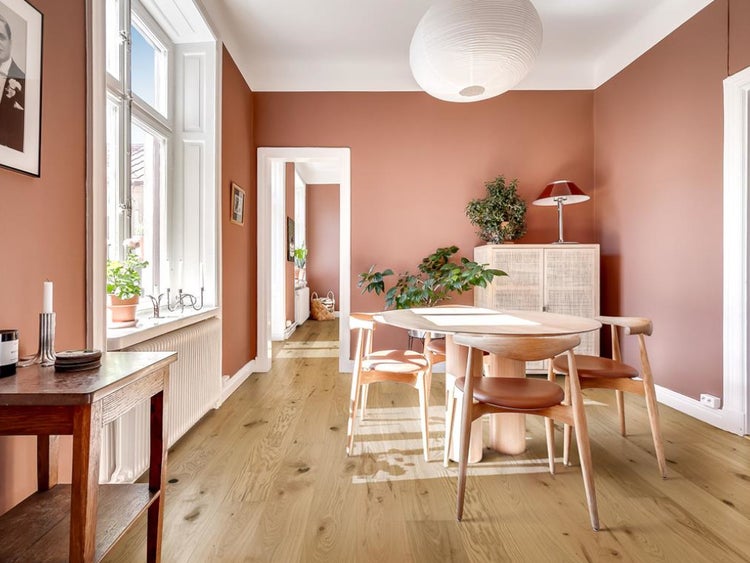 Modernes Esszimmer mit Holzboden in Eichenoptik, runder Sitzgruppe aus Holz, großem Fenster und dekorativen Zimmerpflanzen.