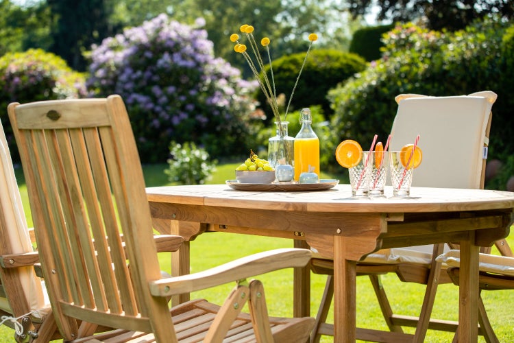 Gartentisch und Stühle aus Teakholz mit Sitzkissen auf einer grünen Wiese für ein entspanntes Ambiente im Freien.