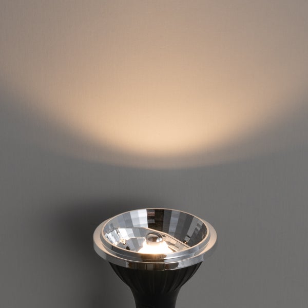 Spotlight-Leuchtmittel mit facettiertem Reflektor wirft einen warmweißen Lichtkegel an eine Wand.