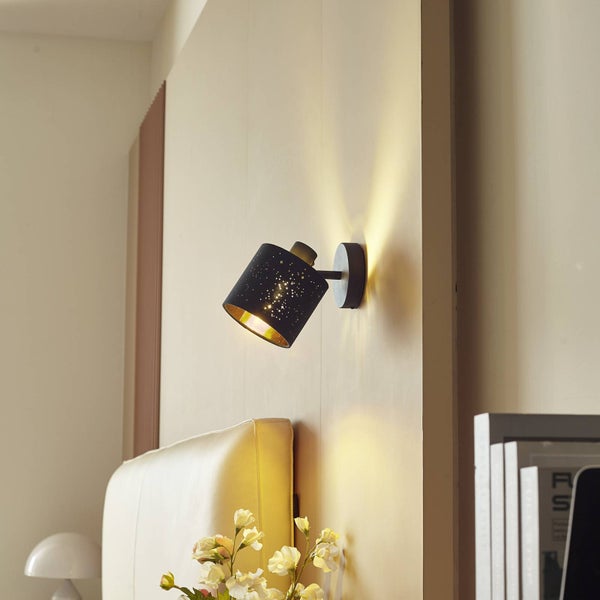 Schwarze Wandleuchte mit Sterneneffekt und goldener Innenseite, montiert im Schlafzimmer über dem Bett.