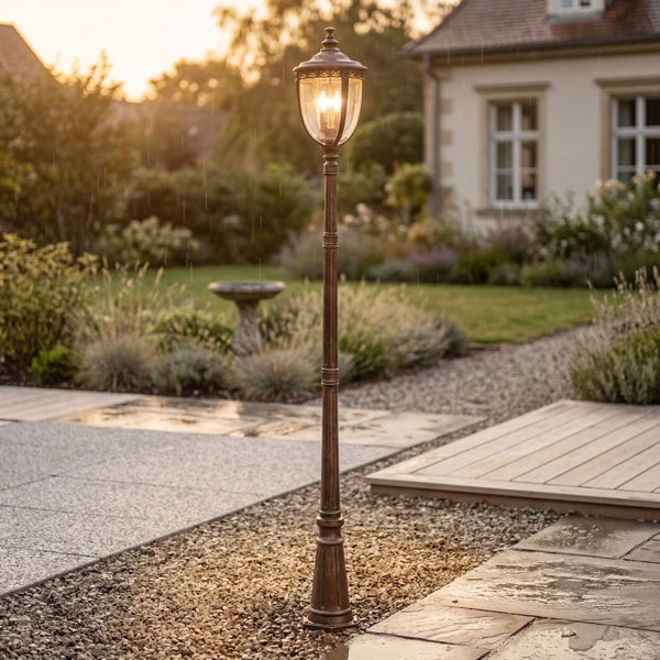 Klassische Außenleuchte im Garten am Wegrand, antik designte Stehlampe mit warmem Licht, Gartenweg mit Kies und Steinplatten im Hintergrund.