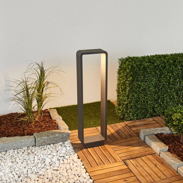 Moderne rechteckige LED-Außenstehleuchte aus Metall in Anthrazit auf einer Holzterrasse in einem organisierten Garten mit Kiesbeet und Hecke.