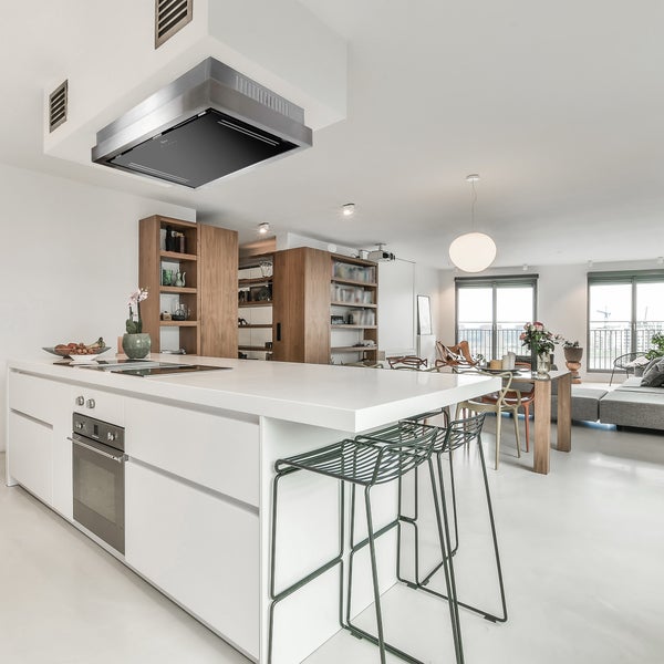 Moderne offene Küche mit weißer Kochinsel, integriertem Backofen, Dunstabzugshaube und angrenzendem Essbereich in einem hellen Wohnraum.