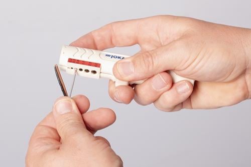 Eine Hand benutzt ein Abisolierwerkzeug an einem Kabel