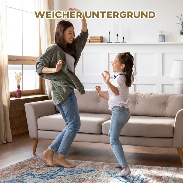 Mutter und Tochter tanzen auf einem gemusterten Teppich in einem Wohnzimmer.