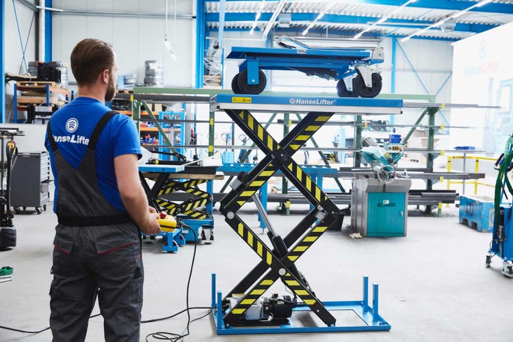 Ein Mitarbeiter bedient eine hydraulische Scherenhubtisch Plattform von HanseLifter mit Kabelfernbedienung in einer Lagerhalle.