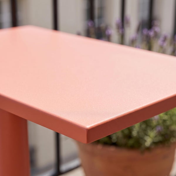 Nahaufnahme der Ecke eines terrakottafarbenen Metalltisches für den Außenbereich mit matter Oberfläche auf einem Balkon.