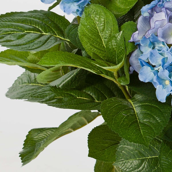 Künstliche Hortensie mit grünen Blättern in einem dunklen Topf.
