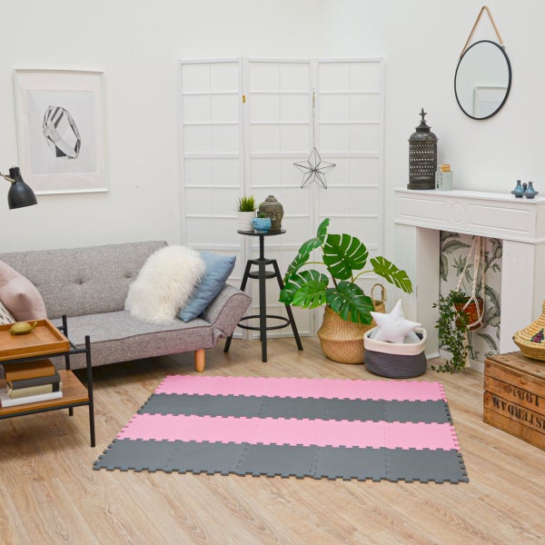 Helles Wohnzimmer mit rosa-grau gestreifter Puzzlematte auf Holzboden, grauem Sofa und weißem Raumteiler sowie dekorativen Elementen.