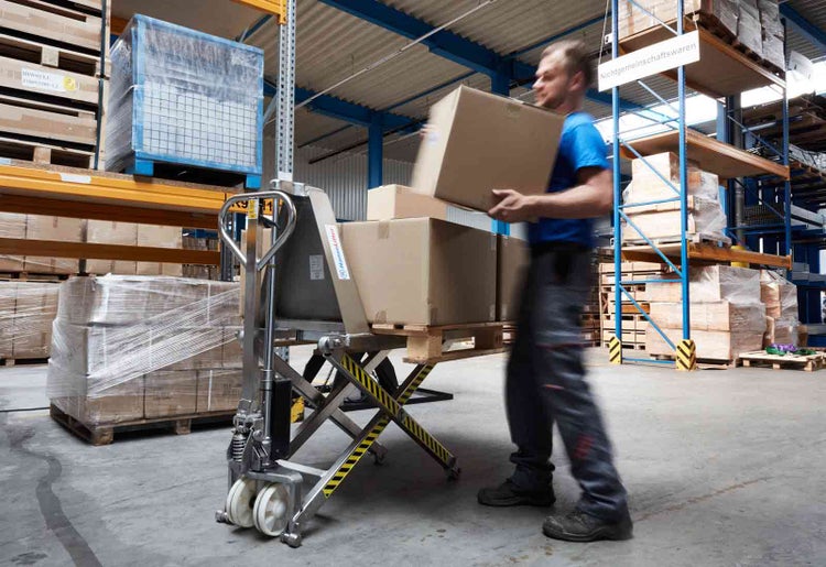 Scherenhubwagen aus Metall im Einsatz in einem Lagerhaus beim Verladen von Kartons auf Paletten.
