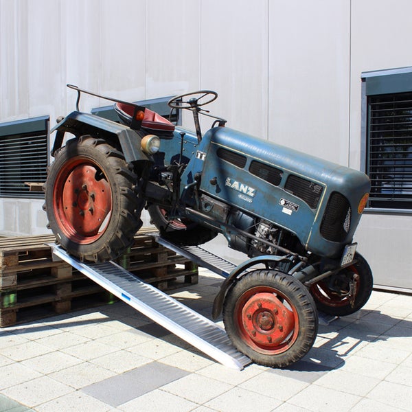 Aluminium-Verladerampen im Einsatz mit einem Traktor auf Holzpaletten vor einer hellen Gebäudewand.
