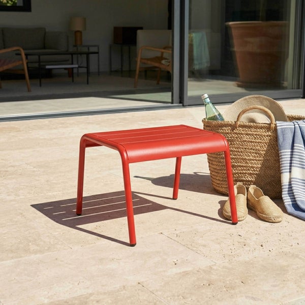 Roter Beistelltisch oder Hocker für den Garten aus Metall mit Lattenoberfläche auf einer Steinterrasse am Pool.