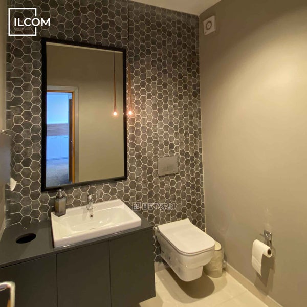 Modernes Badezimmer mit Waschbecken, Spiegel und Toilette vor dekorativer Fliesenwand.