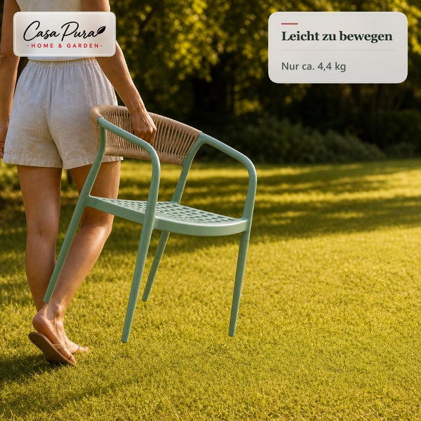 Eine Person trägt einen leichten Gartenstuhl von Casa Pura mit geflochtener Rückenlehne über eine Rasenfläche.