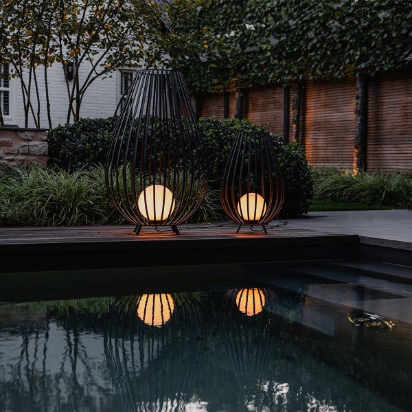 Zwei schwarze Metall Laternenleuchten mit runden Lampen stehen im Garten neben einem Pool.