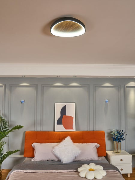 Runde LED Deckenleuchte in Holzoptik in einem modern eingerichteten Schlafzimmer mit Wandpaneel und gepolstertem Bett.