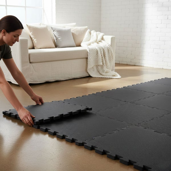 Frau verlegt schwarze, ineinandergreifende Bodenmatten aus Schaumstoff in einem hellen Raum.