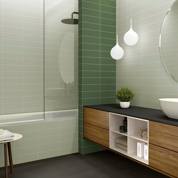 Modernes Badezimmer mit rechteckigen Wandfliesen in verschiedenen Grüntönen, Holzwaschtisch, Badewanne mit Glasduschwand und runden Hängeleuchten.