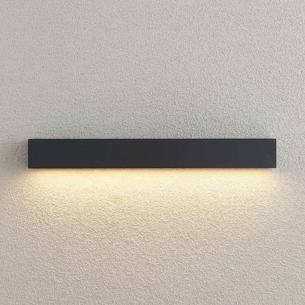 Schwarze, längliche LED Wandleuchte im minimalistischen Design mit indirektem Lichtaustritt nach unten auf einer strukturierten Wandfläche.