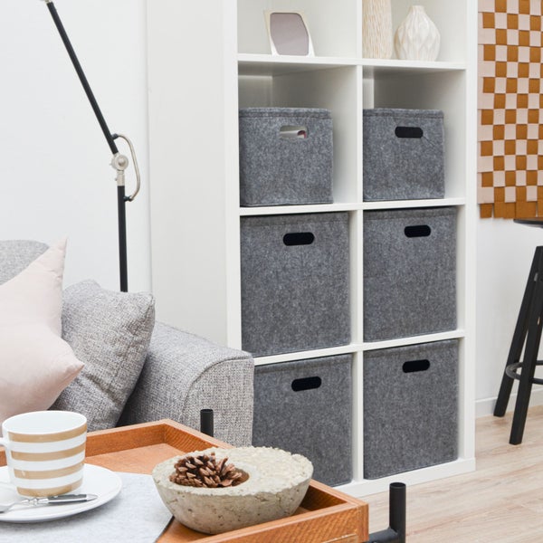Weißes Regal mit sechs grauen Filzboxen als Aufbewahrungselemente im Wohnzimmer neben einem grauen Sofa