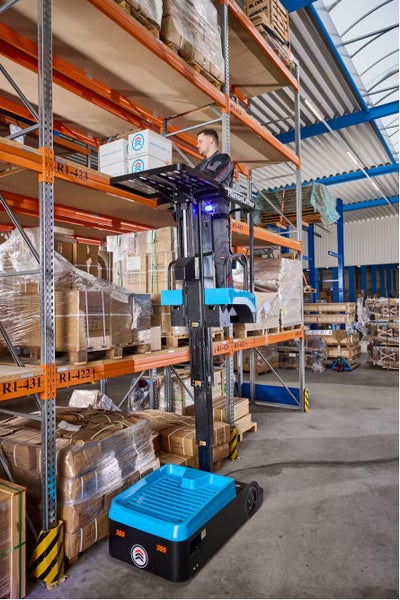 Ein Mitarbeiter bedient einen elektrischen HanseLifter Kommissionierer in einem organisierten Lagerhaus mit hohen Palettenregalen und Kartons.