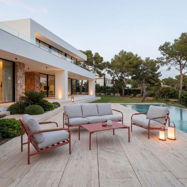 Modernes Garten-Lounge-Set bestehend aus Sofa, zwei Sesseln und einem Couchtisch auf einer Steinterrasse neben einem Pool.