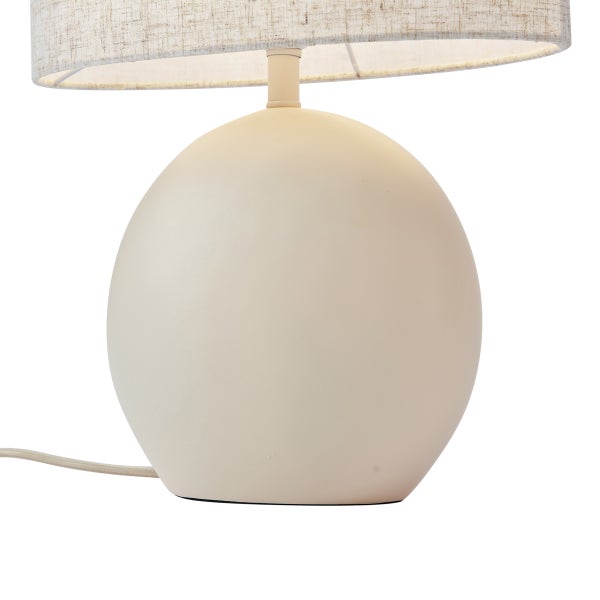 Beige Tischleuchte mit kugelförmigem Fuß und zylindrischem Stoffschirm.