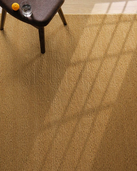 Strukturierter, gewebter Teppich mit Rippenmuster und Flachgewebe, ein Teil eines Hockers steht auf der Oberfläche.