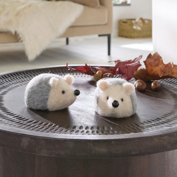 Zwei dekorative Igel Figuren aus Filz auf einem runden dunklen Holztisch arrangiert mit Herbstdekoration wie Blättern und Kastanien.
